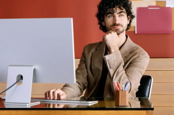 Man sitting at desk with computer, resting chin